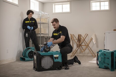 Two ServiceMaster Restore technicians set up drying and dehumidifying equipment in a home after a water damage in the basement