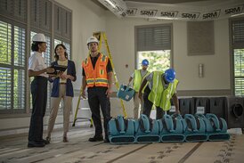 SERVICEMASTER COMMERCIAL RESTORATION MANAGERS DISCUSS A PLAN OF ACTION WITH THE PROPERTY MANAGER AS TECHNICIANS MOVE EQUIPMENT INTO THE BUILDING IN THE BACKGROUND