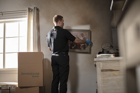 AS THE FIRE TECHNICIAN REMOVES THE FRAMED ART FROM THE WALLS, HE EXPOSES THE WALL UNDERNEATH THE FRAME WHICH IS NOT AFFECTED BY SOOT DAMAGE